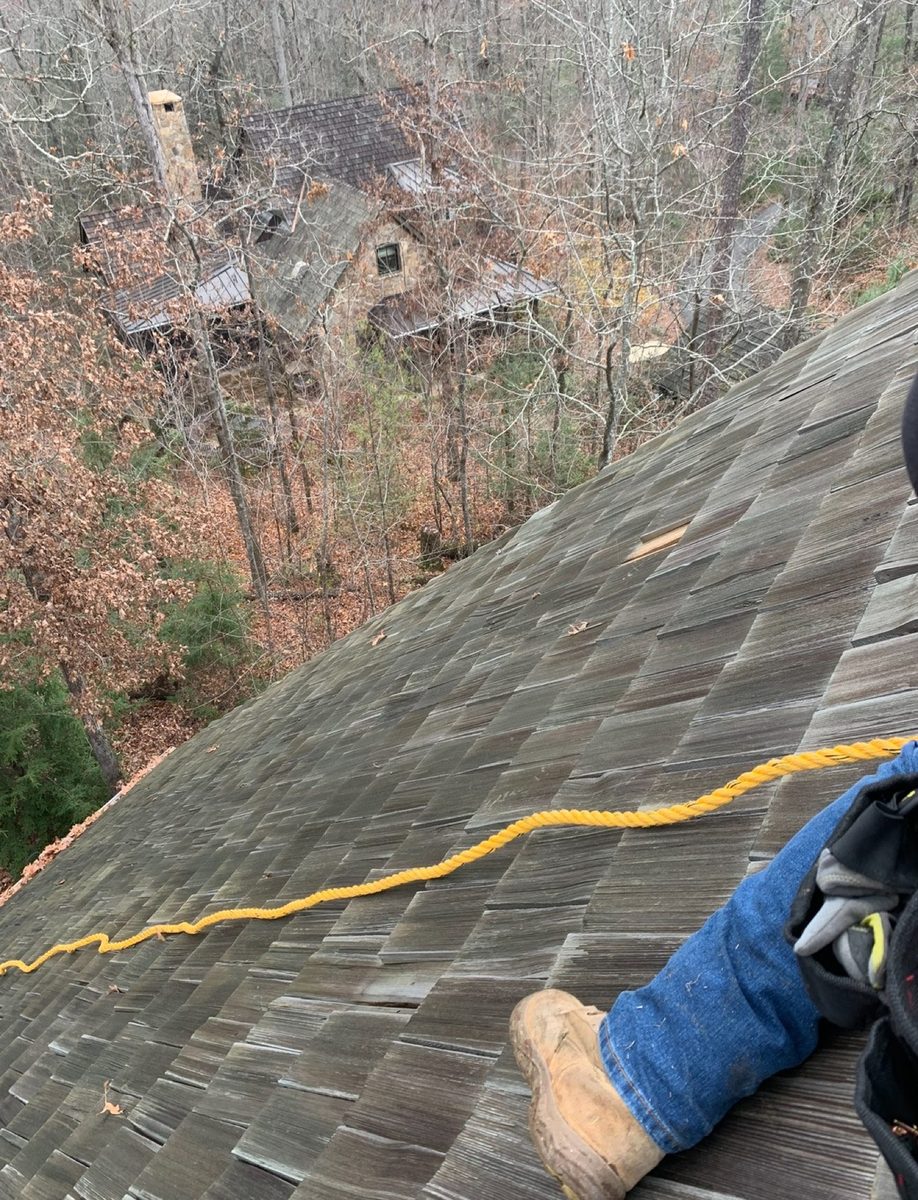 Wood shake roof being inspected from the ridge with a safety line